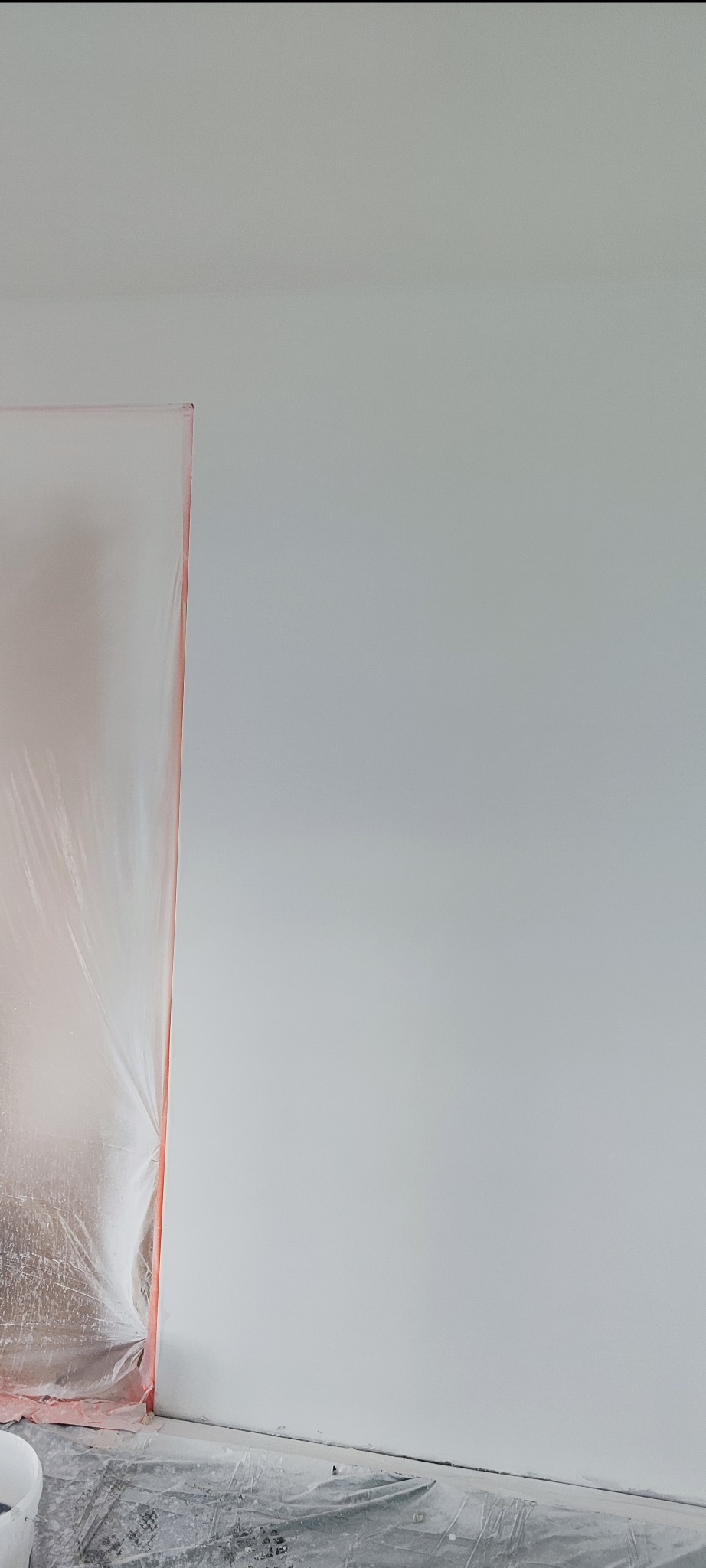 Biała, świeżo pomalowana ściana w pokoju, zabezpieczona folią malarską. Widoczne przygotowania do dalszych prac wykończeniowych.