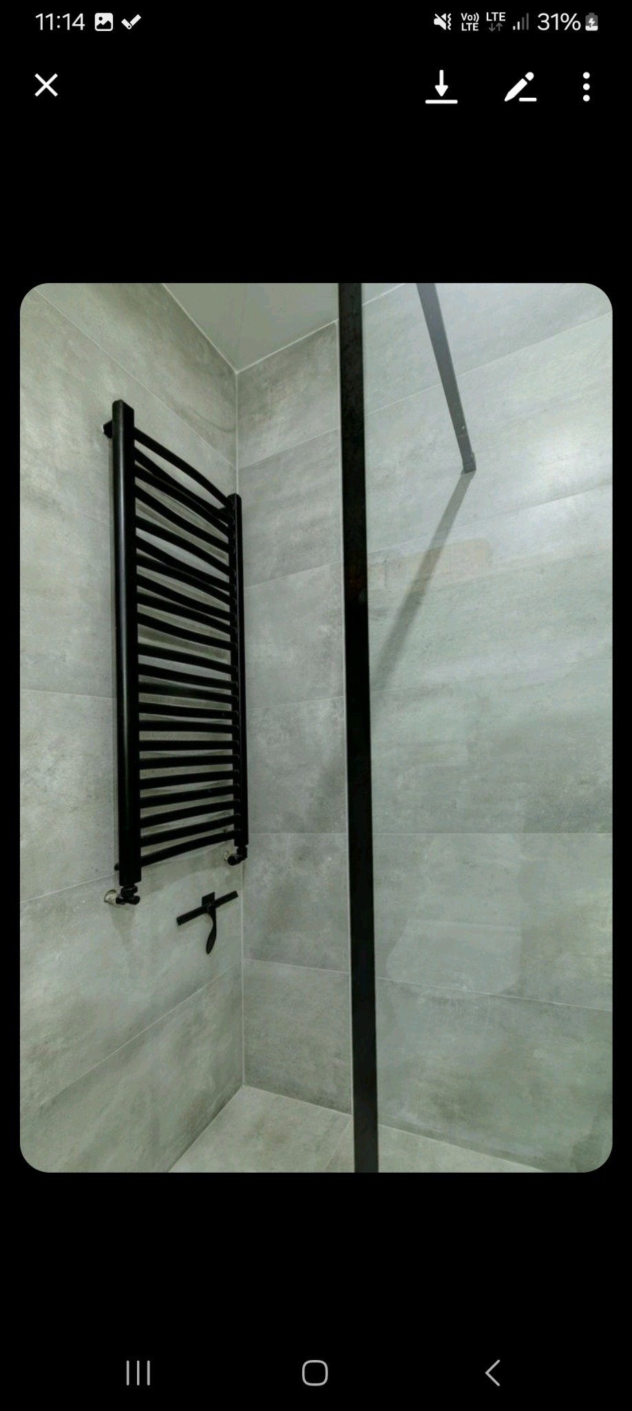 Nowoczesna łazienka z szarymi płytkami imitującymi beton, czarnym grzejnikiem drabinkowym i czarną ramą kabiny prysznicowej.