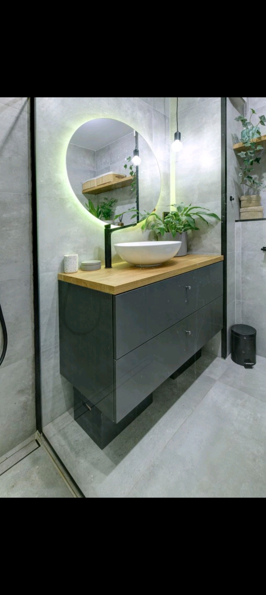 Nowoczesna łazienka z szarą płytką, umywalką nablatową na drewnianym blacie, szafką z szufladami w kolorze grafitowym i okrągłym lustrem z podświetleniem LED.