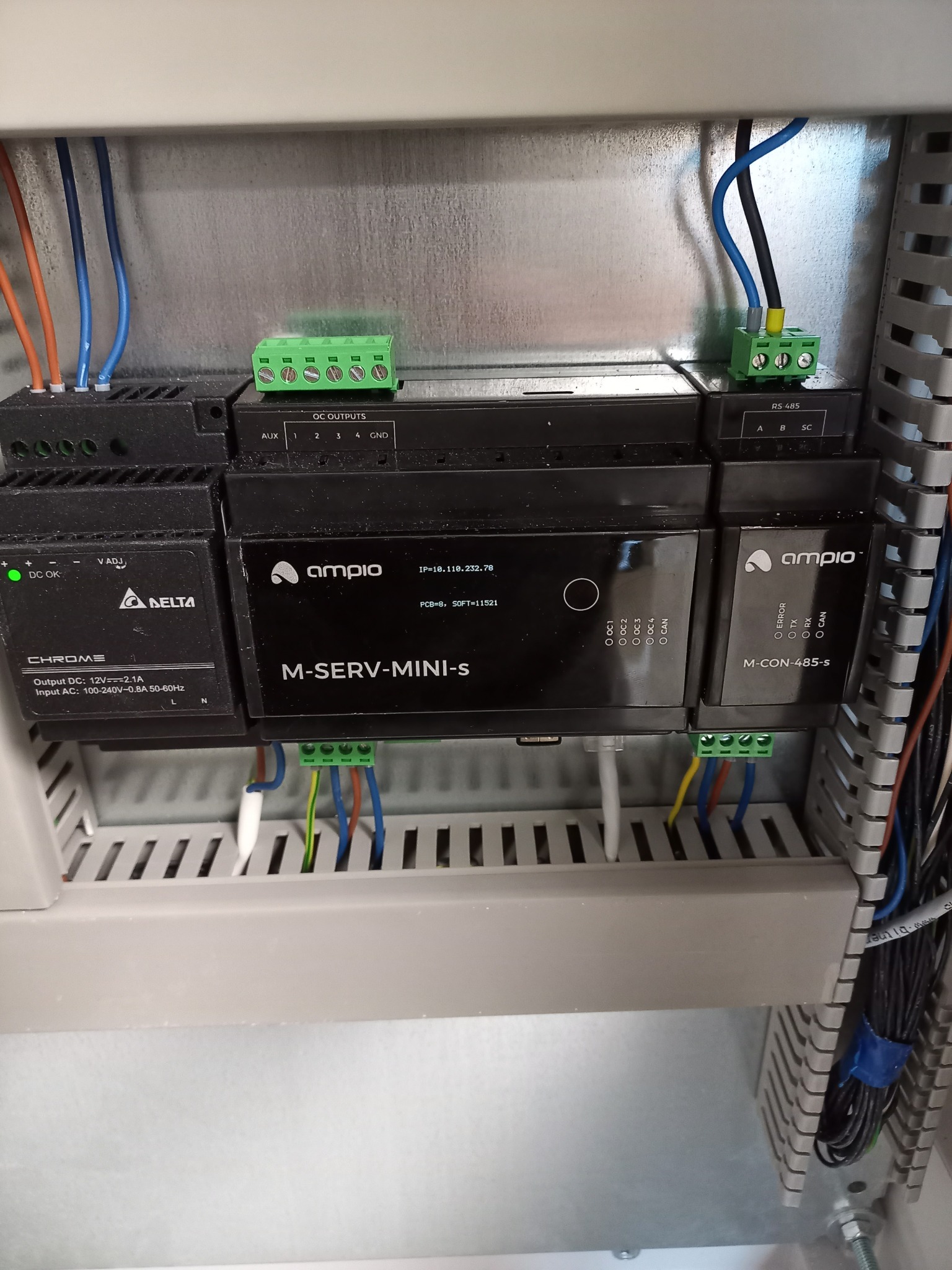 Wnętrze szafy sterowniczej z modułami elektronicznymi firmy Ampio, widoczne zasilacze Delta Chrome, moduł M-SERV-MINI-S z adresem IP, oraz moduł M-CON-485-S, okablowanie z użyciem zielonych złączek...