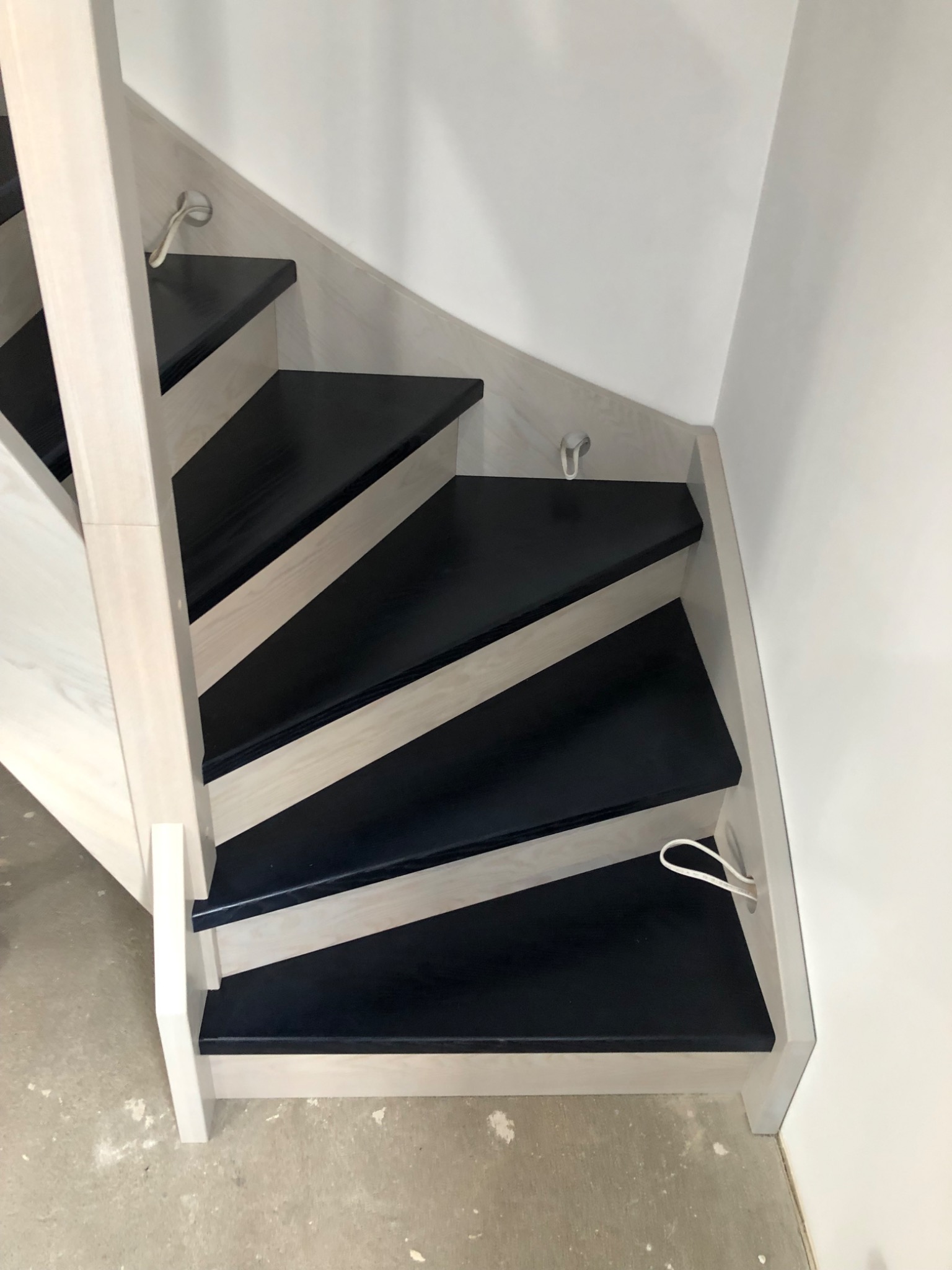 Nowoczesne schody drewniane z czarnymi stopniami i jasnymi bokami, widok z góry na kilka stopni i fragment ściany.