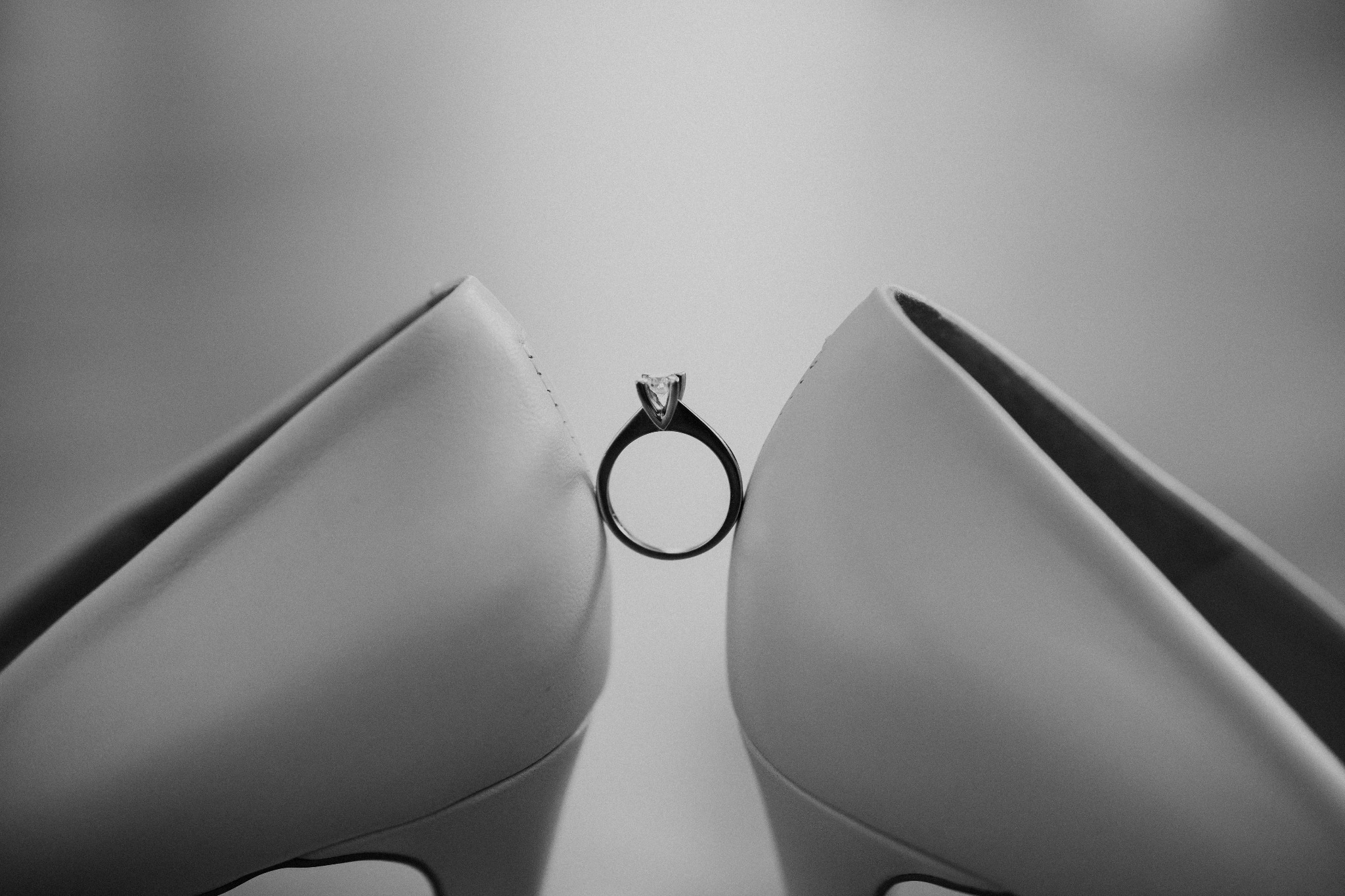 Czarno-białe zbliżenie pary damskich szpilek z pierścionkiem zaręczynowym z diamentem umieszczonym między nimi.