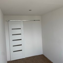 Graf Transport-Remonty - Wnętrze pokoju po remoncie z przesuwnymi drzwiami w kolorze białym z poziomymi przeszkleniami, zamontowanymi na metalowej szynie. Na podłodze panele imitujące drewno.