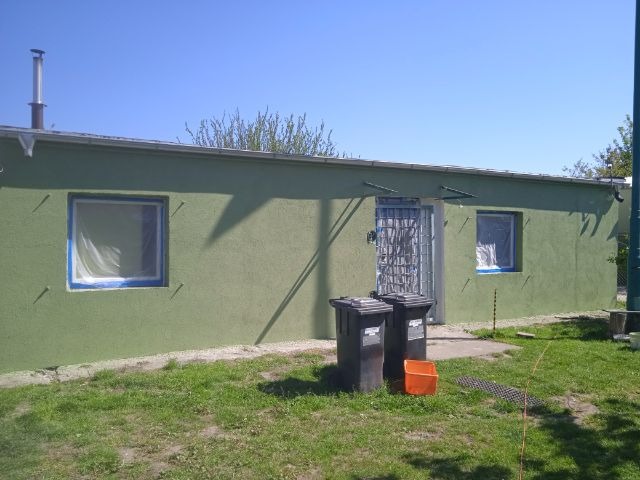 Budynek z zieloną elewacją we Wrocławiu, okna zabezpieczone folią i taśmą malarską, dwie czarne beczki na śmieci i pomarańczowe wiadro przed wejściem.