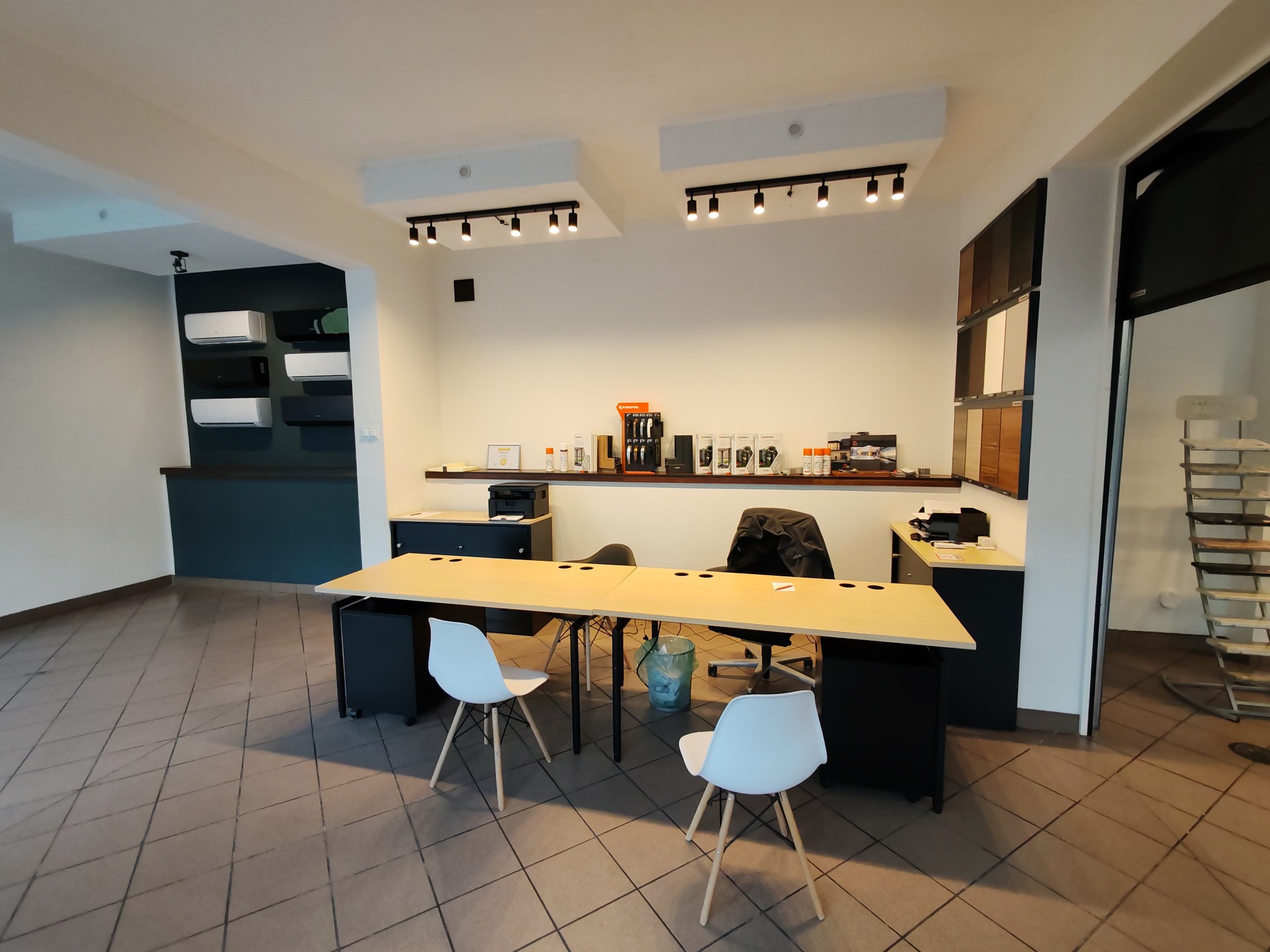 Wnętrze biura z ekspozycją próbek stolarki otworowej, widoczne biurka, krzesła i regał z próbkami kolorów i materiałów.