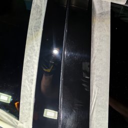 GregorDetailing - Detailing samochodu: polerowanie czarnych słupków karoserii, zabezpieczonych taśmą maskującą, z użyciem latarki inspekcyjnej do uwidocznienia rys.