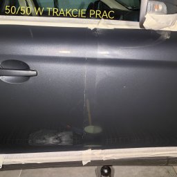 GregorDetailing - Część karoserii samochodu w trakcie polerowania, widoczna różnica w połysku między obszarem po lewej i prawej stronie, zabezpieczona taśmą malarską, napis '50/50 W TRAKCIE PRAC' na szybie.