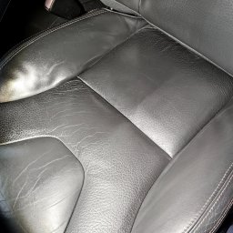 GregorDetailing - Fragment czarnego skórzanego fotela samochodowego z widocznymi śladami użytkowania i zapięciem pasów bezpieczeństwa.