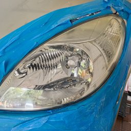 GregorDetailing - Reflektor samochodowy oklejony niebieską taśmą malarską przed renowacją w Jeleniej Górze, widoczny fragment karoserii.