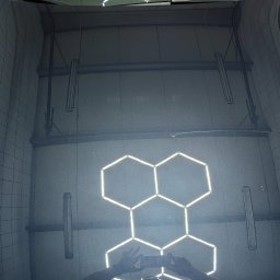 GregorDetailing - Błyszcząca, czarna karoseria samochodu odbija sufit myjni z heksagonalnym oświetleniem LED i elementami konstrukcyjnymi, z widocznymi rękoma robiącymi zdjęcie.