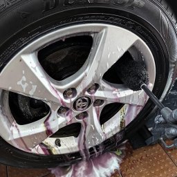 GregorDetailing - Czyszczenie aluminiowej felgi samochodowej szczotką, spływający fioletowy płyn z pianą na brązową kostkę brukową.