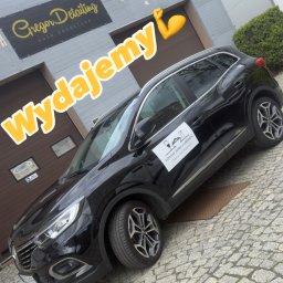 GregorDetailing - Czarny SUV po detailingu przed budynkiem z szyldem 'Gregor Detailing', z naklejką restauracji na drzwiach. Ujęcie z dołu, z żółtym napisem 'Wydajemy'.