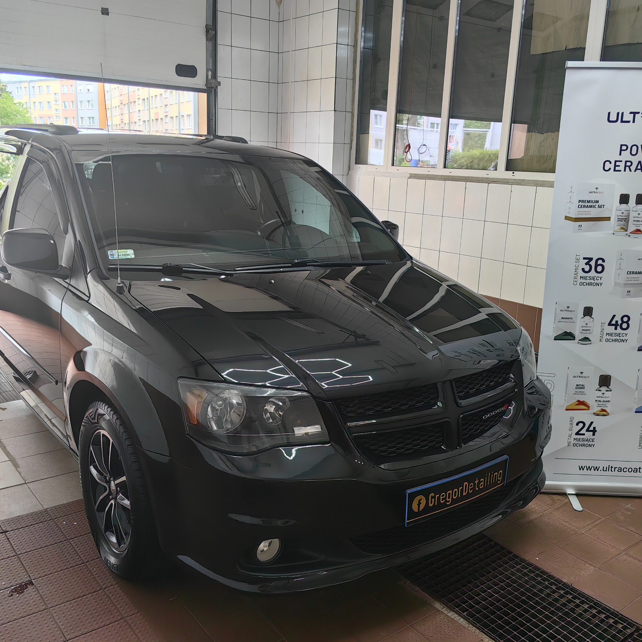 Błyszczący, czarny Dodge Caravan po detailingu, z widocznym logo firmy GregorDetailing na tablicy rejestracyjnej, w tle reklama powłok ceramicznych UltraCoat i białe kafelki myjni.