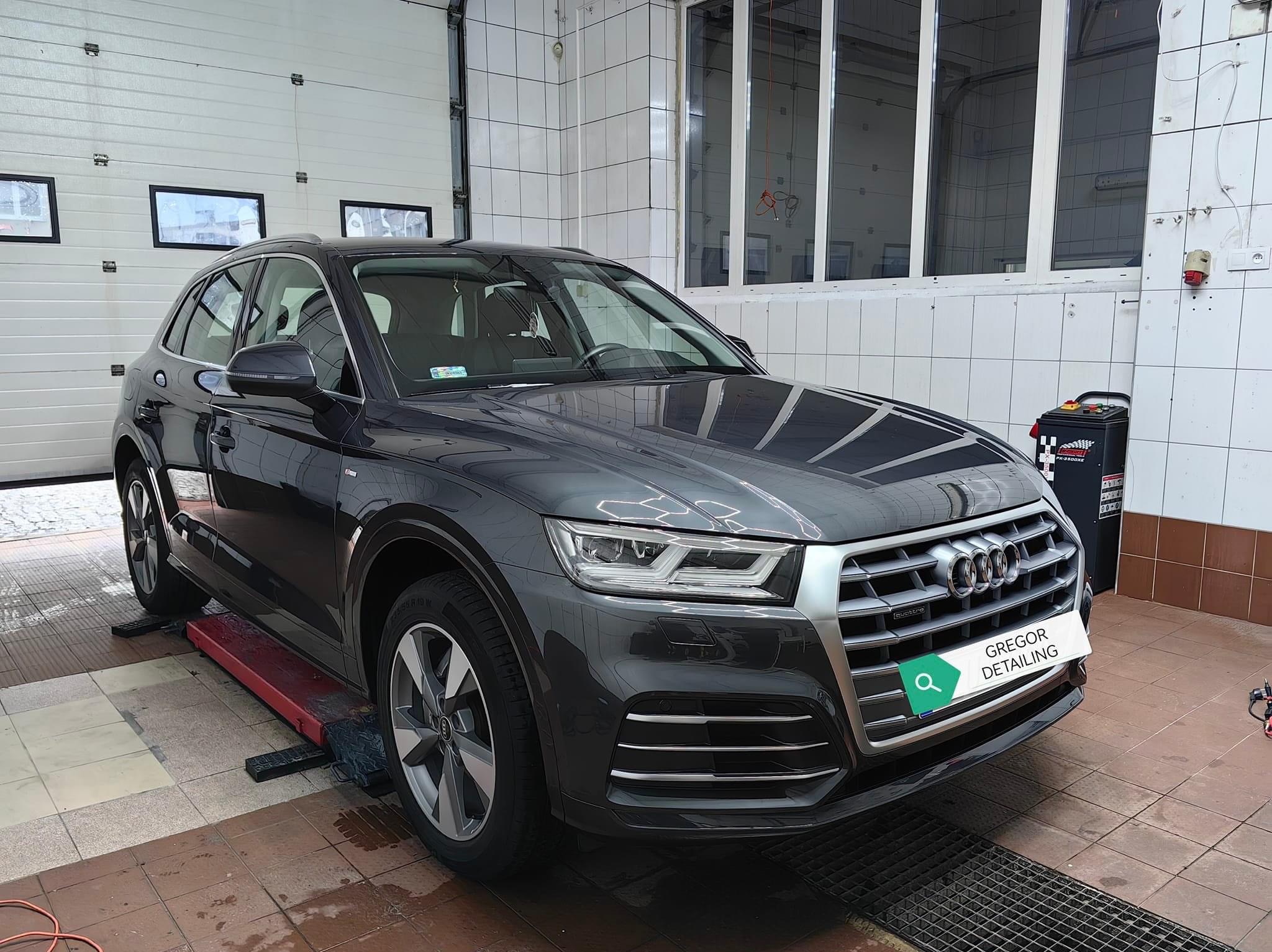 Ciemnoszary Audi Q5 na podnośniku w myjni, widoczny sprzęt do detailingu i logo firmy Gregor Detailing na przednim zderzaku.