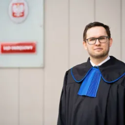 Portret mężczyzny w todze adwokackiej na tle budynku sądu z godłem Polski.