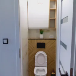 Nowoczesna toaleta z drewnianą mozaiką na ścianie, białą szafką nad muszlą i otwartą półką obok, widok zza częściowo otwartych białych drzwi z czarną klamką.