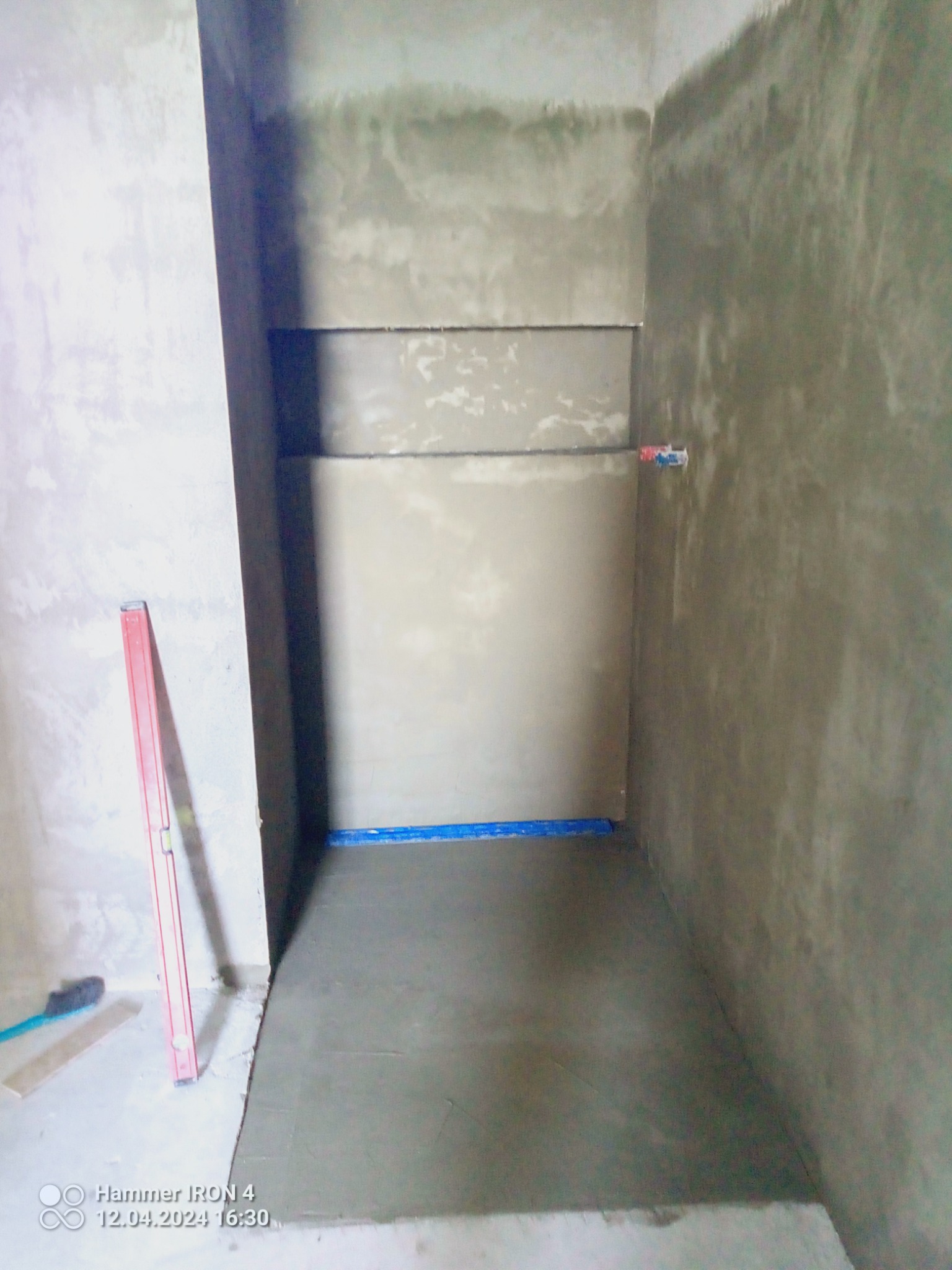 Przygotowanie do położenia płytek w kabinie prysznicowej: wyrównane ściany z wnękami, wylewka podłogowa, poziomica oparta o ścianę, widoczny odpływ liniowy.