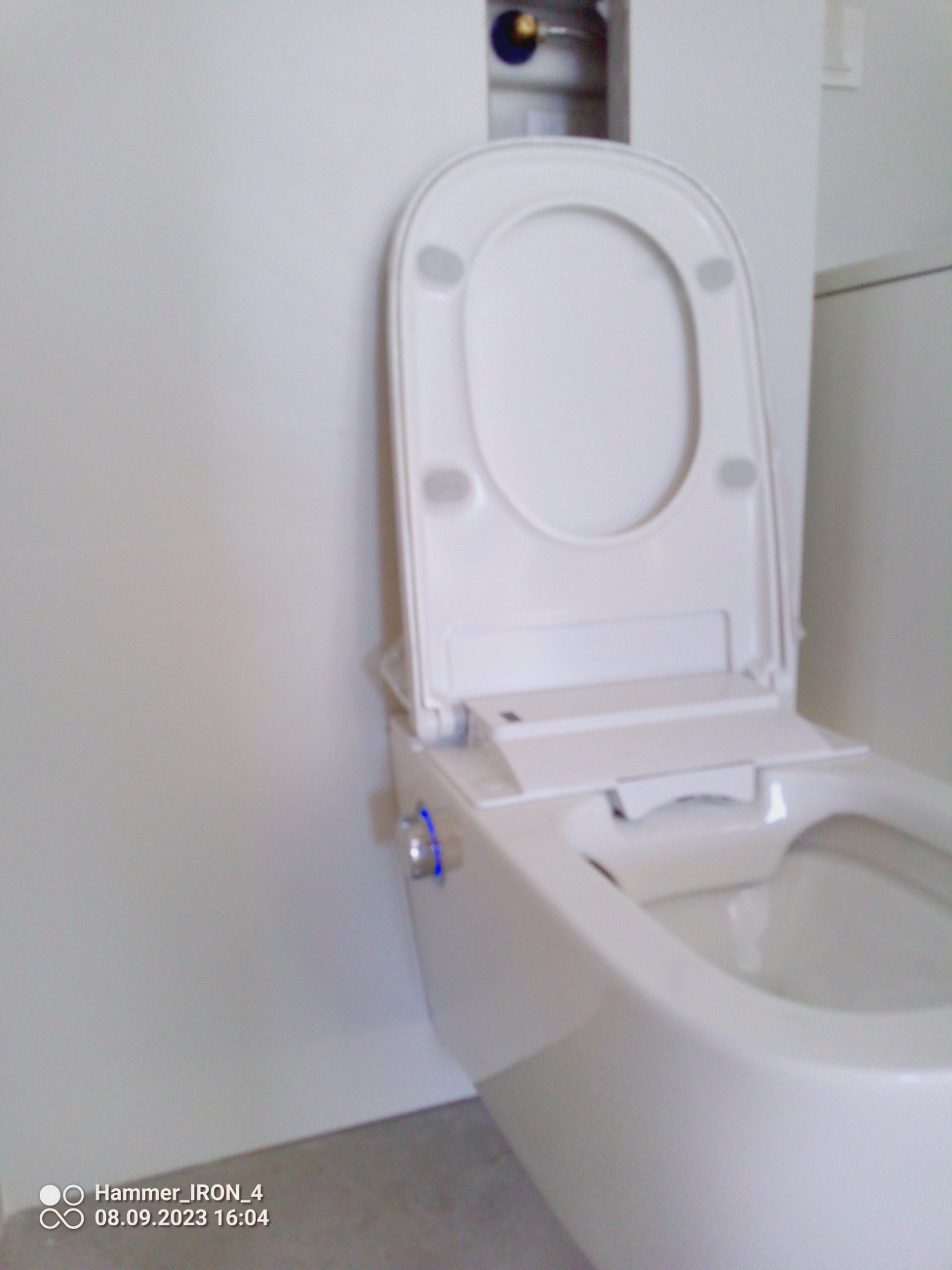 Nowoczesna, biała toaleta wisząca z funkcją bidetu i podświetlanym panelem sterowania, zamontowana w minimalistycznej łazience z białymi ścianami.