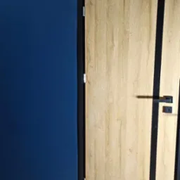 Nowoczesne drzwi wewnętrzne z drewnopodobnym wykończeniem i czarnymi wstawkami na tle granatowej ściany i drewnianej podłogi, widoczne akcesoria montażowe w rogu.