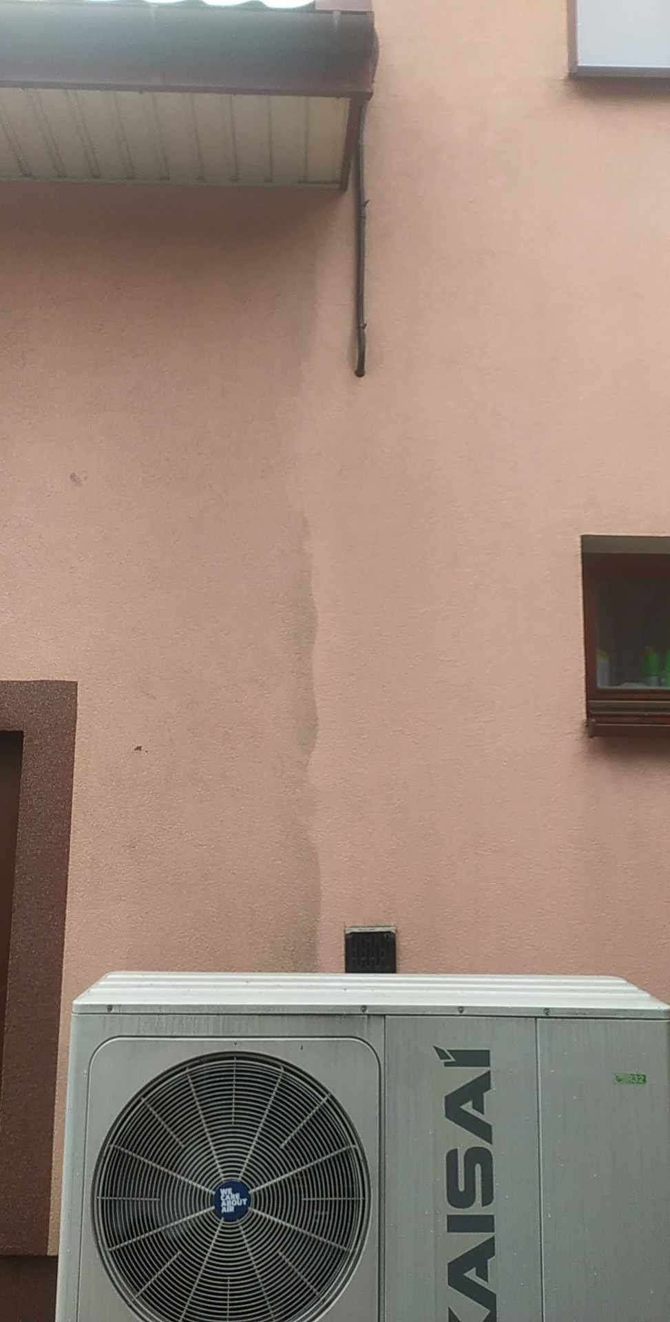 Brudna, różowa elewacja budynku z widocznym śladem po spływającej wodzie, poniżej zamontowana jednostka zewnętrzna klimatyzacji marki Kaisai.
