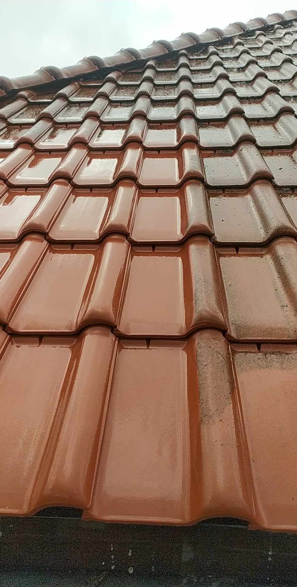 Czerwona dachówka ceramiczna, część dachu jest czysta, a część pokryta brudem, widoczne krople wody.