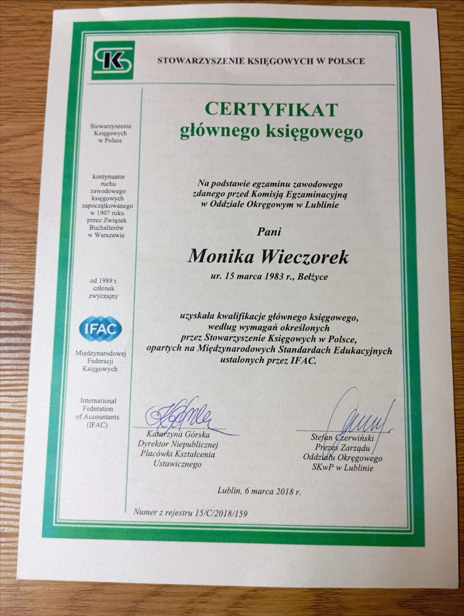 Certyfikat głównego księgowego wydany przez Stowarzyszenie Księgowych w Polsce, z podpisami i pieczęciami, na drewnianym biurku.