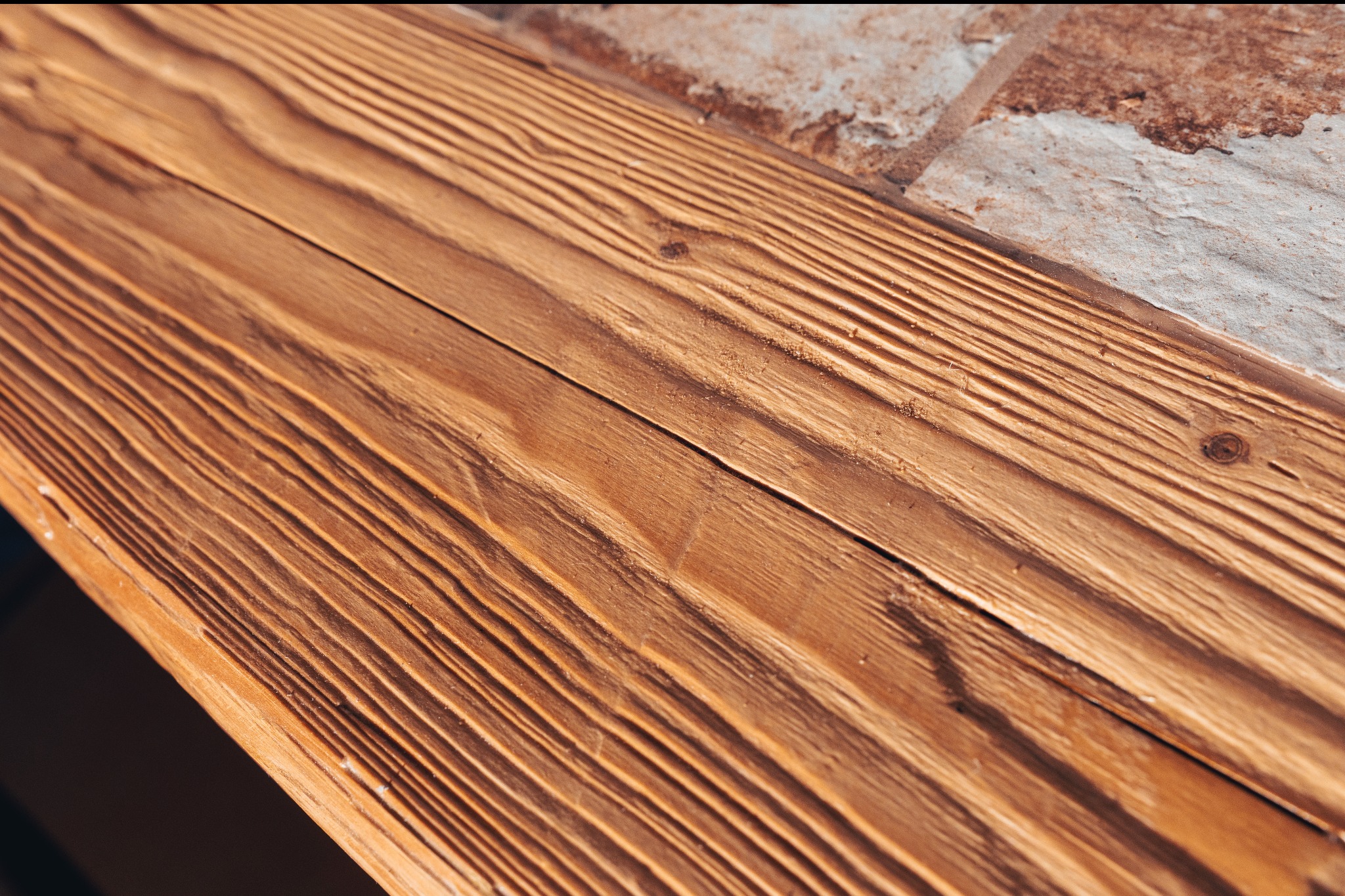 Fragment drewnianej konstrukcji z wyraźnym usłojeniem, połączonej z elementami kamiennymi o nieregularnej fakturze. Ujęcie z bliska, podkreślające detale materiałów.