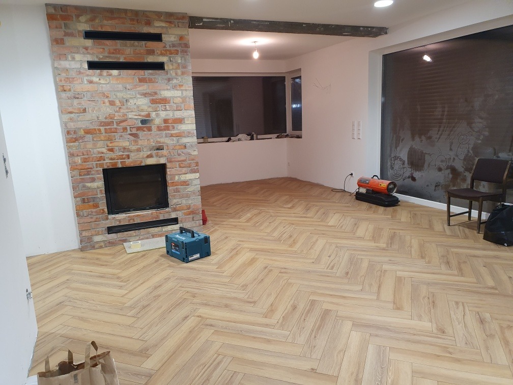 Salon z nowo ułożonym parkietem w jodełkę, ceglanym kominkiem z czarnym wkładem, nagrzewnicą i zakrytymi oknami