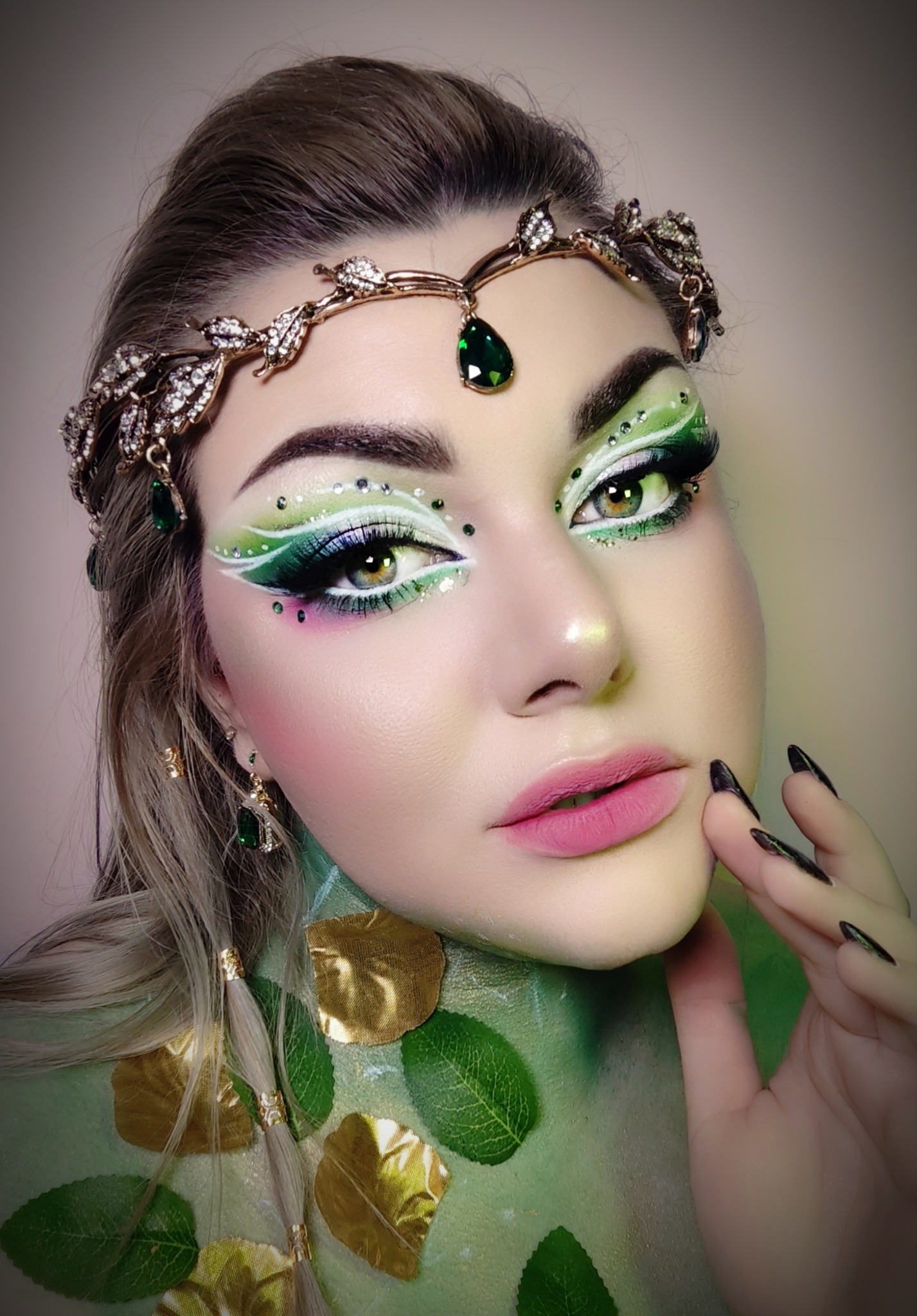 Portret kobiety z artystycznym, zielono-białym zdobieniem powiek, kryształkami i ozdobną biżuterią na głowie, stylizowaną na leśną nimfę.