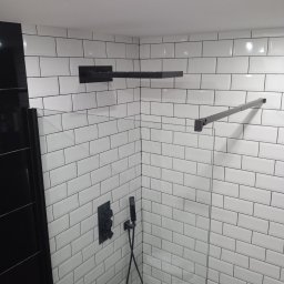 Filip Zawadzki - Nowoczesna kabina prysznicowa z białymi, prostokątnymi płytkami ułożonymi w cegiełkę, czarna armatura i szklane drzwi, minimalistyczny design.