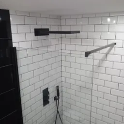 Nowoczesna kabina prysznicowa z białymi, prostokątnymi płytkami ułożonymi w cegiełkę, czarna armatura i szklane drzwi, minimalistyczny design.