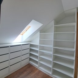MEBLE SZNAJDER BARTŁOMIEJ SZNAJDER - Biała zabudowa w skosach poddasza: szafa z półkami i komoda z szufladami, drewniana podłoga, okno dachowe.