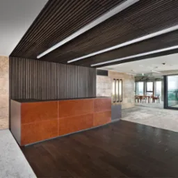 Recepcja biurowa z brązową ladą, drewnianym sufitem lamelowym i kamienną ścianą z podłużnymi lampami.