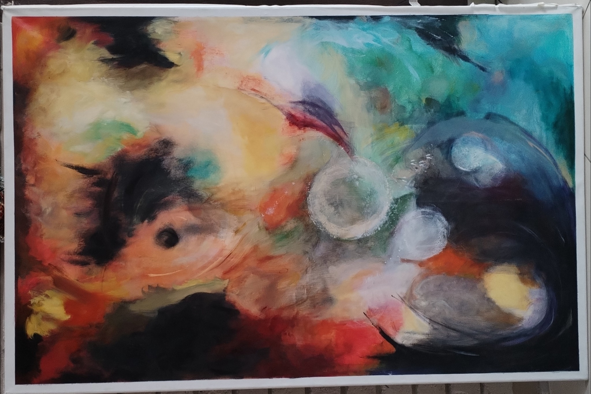 Abstrakcyjne malowidło na płótnie z przewagą ciepłych barw, z widocznymi okrągłymi elementami i mocnymi pociągnięciami pędzla, oprawione w białą ramę.