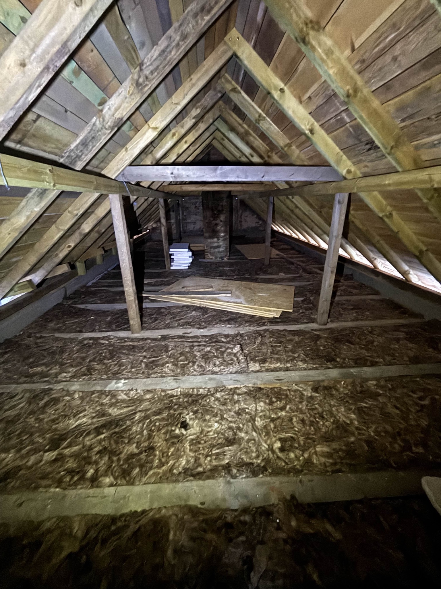 Poddasze z widoczną izolacją z wełny mineralnej między krokwiami, przygotowane do dalszych prac wykończeniowych. Widoczne deski i elementy konstrukcji dachu.