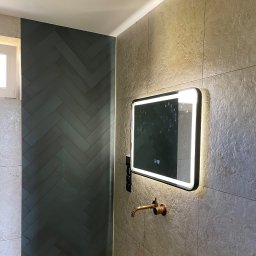 Daniel Cisek - Nowoczesna łazienka z szarymi płytkami ułożonymi w jodełkę, podświetlane lustro z dotykowym panelem i miedziana bateria umywalkowa.