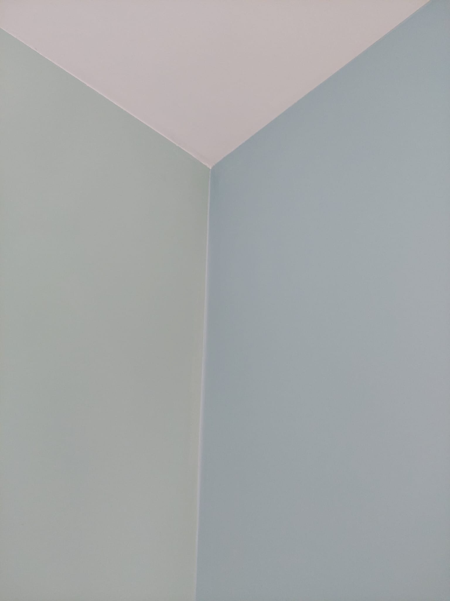 Pomieszczenie po świeżym malowaniu, ściany w odcieniach błękitu i szaro-zieleni, sufit biały, widoczny narożnik.