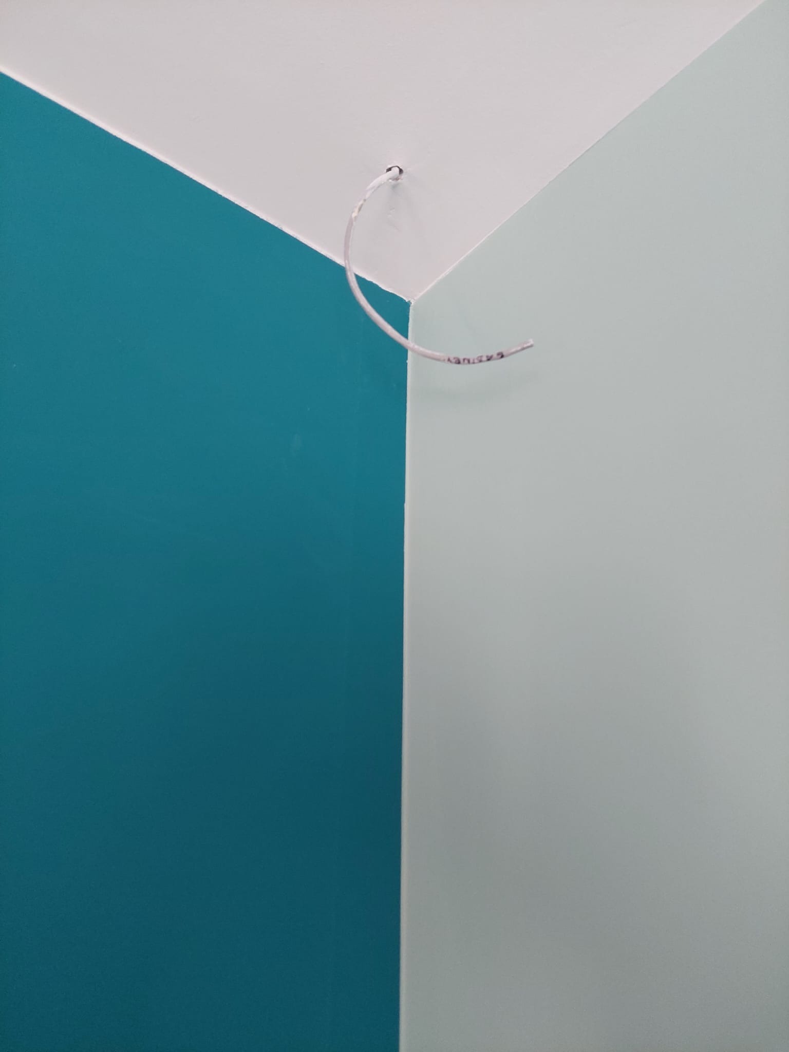 Ściana pomalowana na dwa kolory: turkusowy i jasnoszary, z wystającym kablem elektrycznym przy suficie.