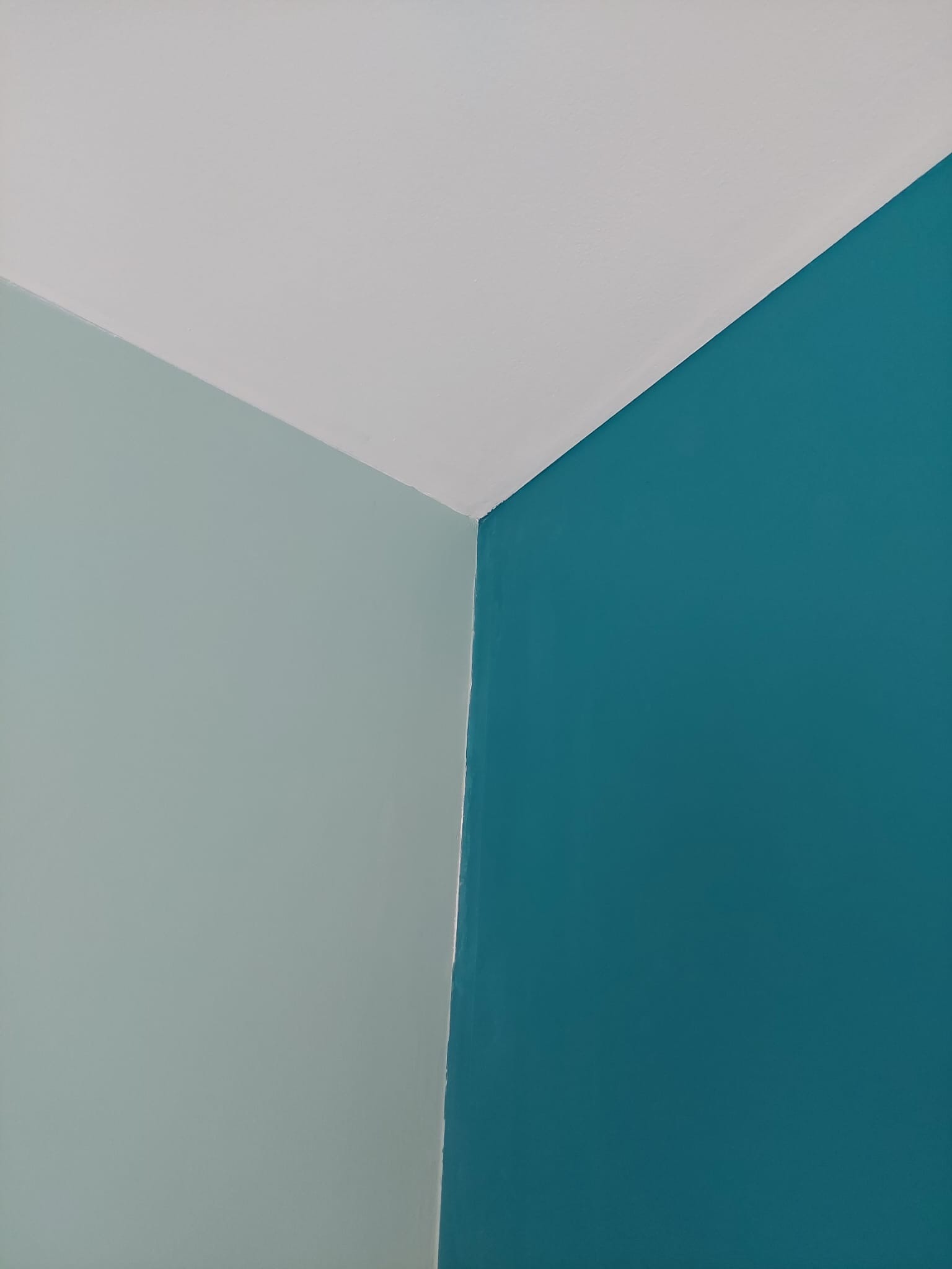 Świeżo pomalowany narożnik pokoju z trzema kolorami: biały sufit, turkusowa ściana i jasnozielona ściana.