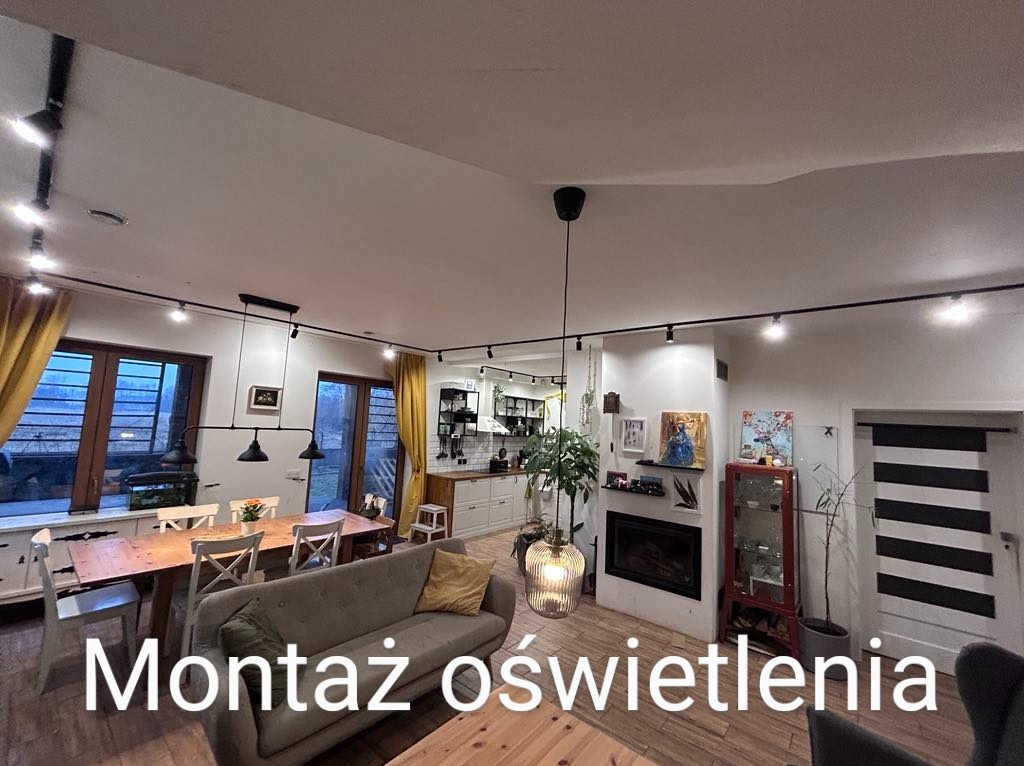 Salon z zamontowanym systemem szynowym oświetlenia punktowego, oświetlającym stół jadalny i przestrzeń wypoczynkową z kominkiem.