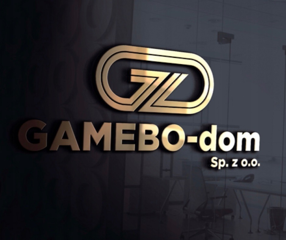 Złote logo firmy GAMEBO-dom Sp. z o.o. na ciemnym, błyszczącym tle ściany biura. Logo składa się z inicjałów GZ wewnątrz zaokrąglonej ramki. W tle widoczne biurko i krzesło.