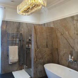 MERIDIAN EU SPÓŁKA Z OGRANICZONĄ ODPOWIEDZIALNOŚCIĄ - Nowoczesna łazienka z marmurowymi płytkami, wolnostojącą białą wanną i designerskim, kryształowym żyrandolem w kształcie prostokąta.