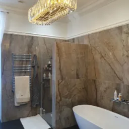 Nowoczesna łazienka z marmurowymi płytkami, wolnostojącą białą wanną i designerskim, kryształowym żyrandolem w kształcie prostokąta.