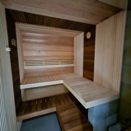 MERIDIAN EU SPÓŁKA Z OGRANICZONĄ ODPOWIEDZIALNOŚCIĄ - Nowoczesna sauna z jasnego drewna z elementami z ciemniejszego drewna, wielopoziomowe ławki, oświetlenie punktowe, widok z góry.