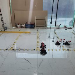 MERIDIAN EU SPÓŁKA Z OGRANICZONĄ ODPOWIEDZIALNOŚCIĄ - Montaż białych płytek podłogowych z marmurowym wzorem, przy użyciu przyssawek i poziomicy, widoczne żółte klipsy do poziomowania.