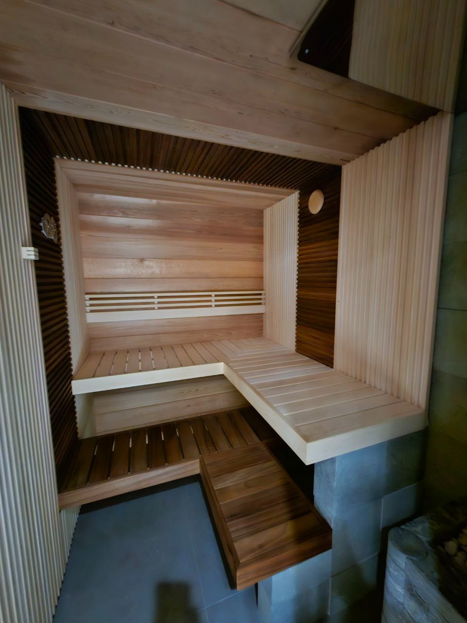 Nowoczesna sauna z jasnego drewna z elementami z ciemniejszego drewna, wielopoziomowe ławki, oświetlenie punktowe, widok z góry.