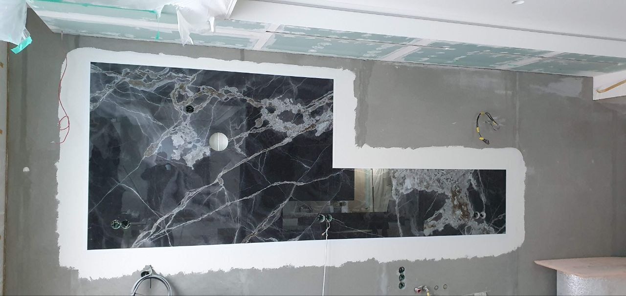 Montaż paneli z czarnego marmuru z białymi żyłami na ścianie w trakcie prac wykończeniowych, widoczne wystające kable elektryczne i surowy tynk.