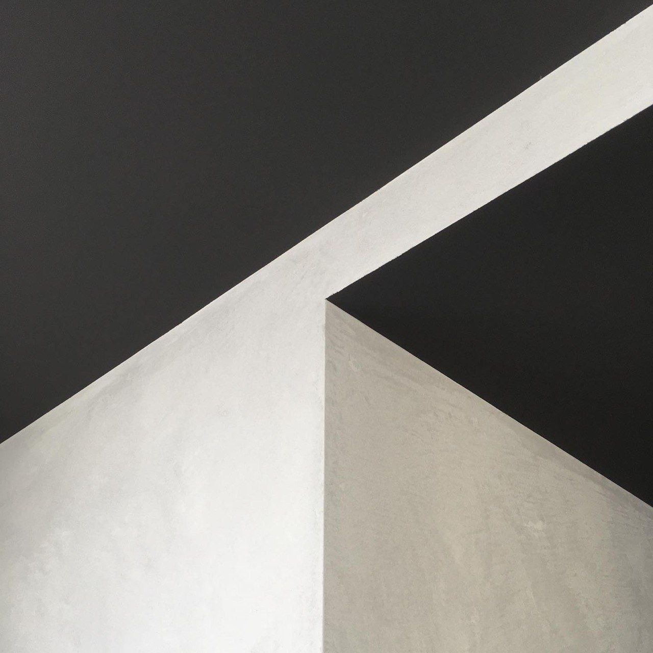 Kontrastowe połączenie gładzi w odcieniach bieli i szarości z czarnym sufitem, podkreślone ukośną, białą linią, tworzące minimalistyczny, geometryczny design wnętrza.