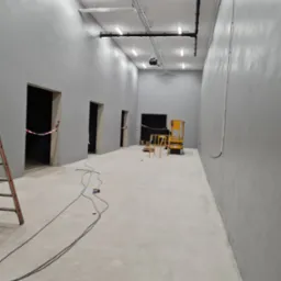 Wnętrze biura po malowaniu ścian na szaro, widoczny podnośnik koszowy, przewody na podłodze i zabezpieczone taśmą wejścia do pomieszczeń.