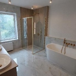 MAGRA Izabella Kalinowska - Luksusowa łazienka z marmurowymi ścianami i podłogą, kabina prysznicowa ze złotymi detalami, wolnostojąca wanna z baterią ścienną, dwie umywalki nablatowe z armaturą w kolorze złota, oświetlenie...